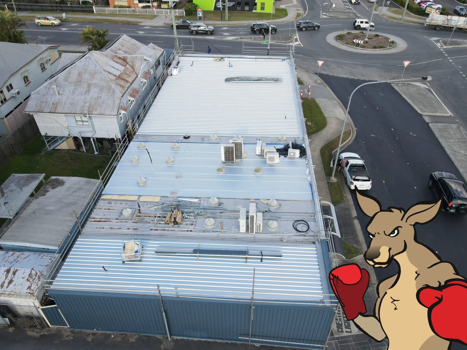 Aerial view of a commercial metal roof replacement in progress, with the Southern Cross Roofing kangaroo in the foreground.